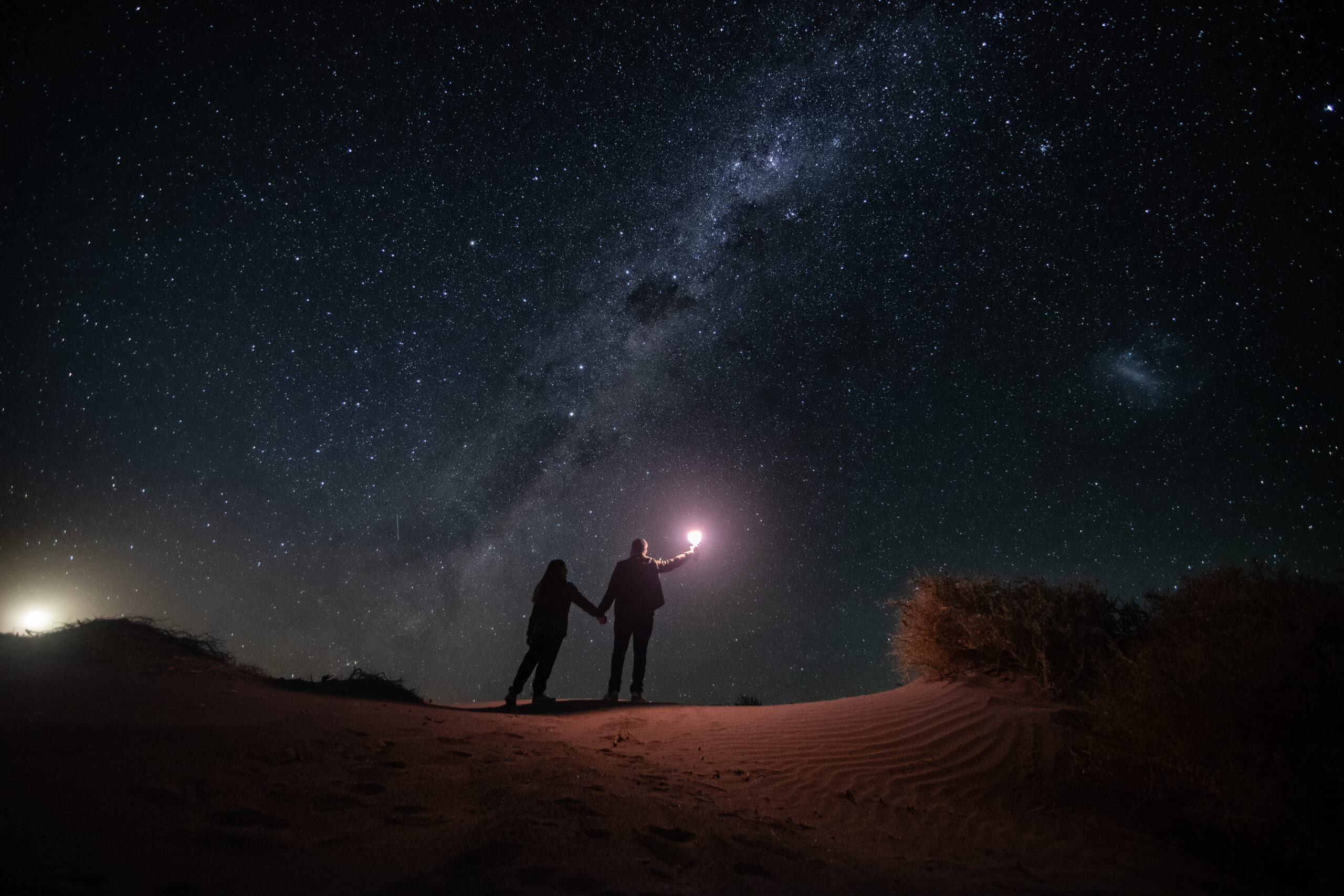 Foto de pareja en el desierto sosteniendo una luz bajo la vía láctea