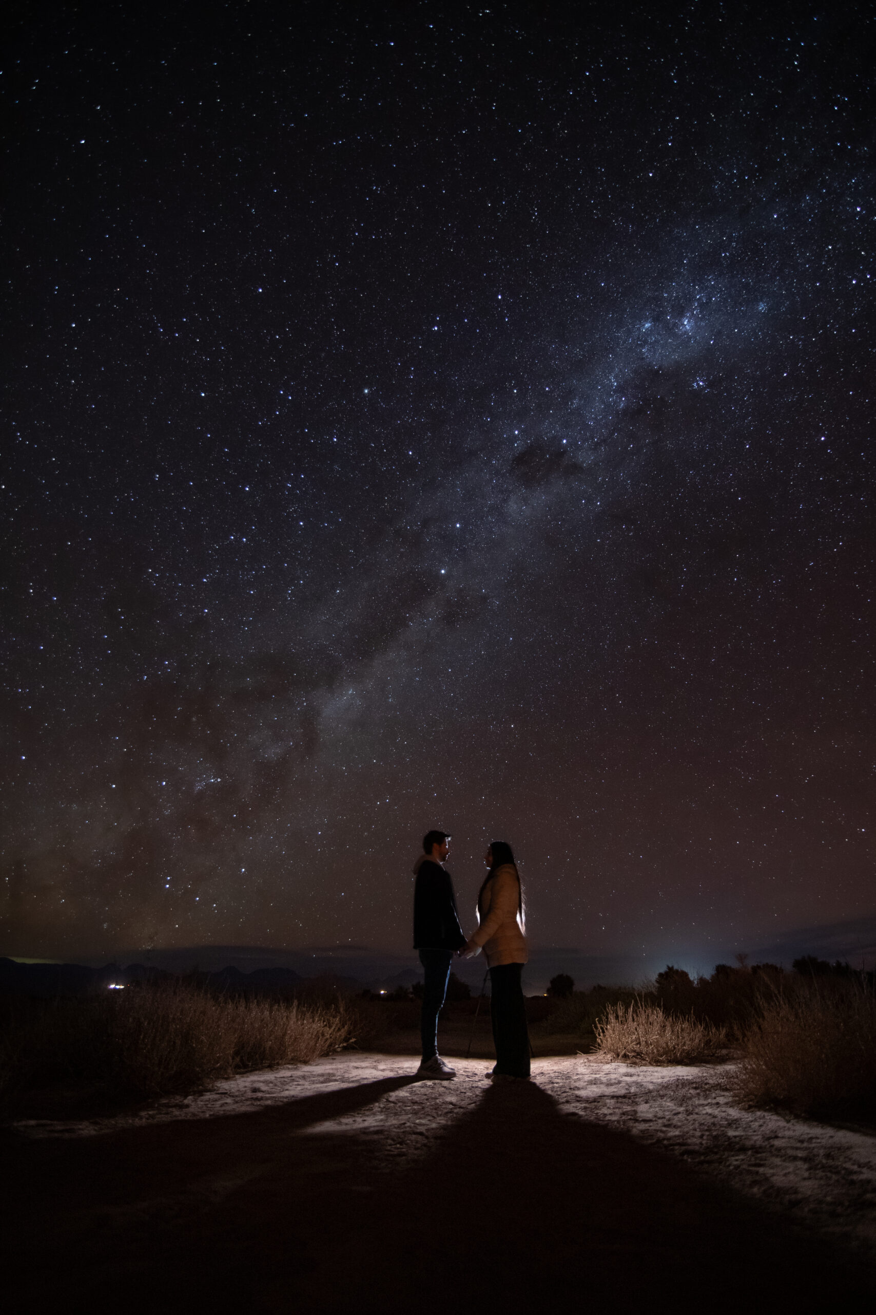 Foto de pareja tomandose las manos a contraluz con la vía láctea